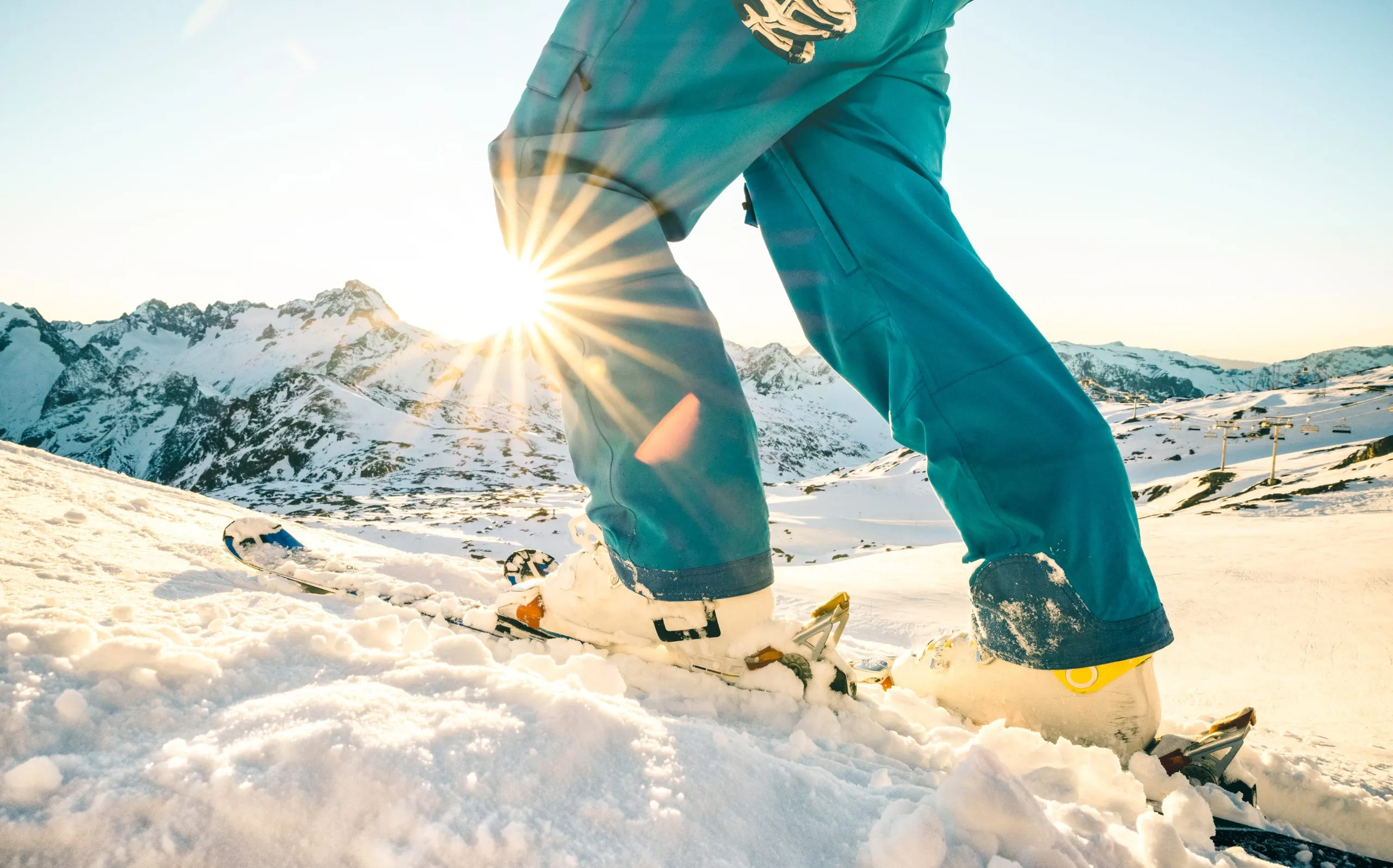 Legs of professional skier at sunset on relax moment in french alps ski resort - Winter sport concept with adventure guy on mountain top ready to ride down - Side view point with azure vintage filter