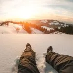 Pov of young man looking the sunset on snow high mountains - Winter vacation concept - Focus on his feet