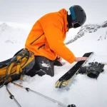 Ski tourist repairs skis in snowy mountains. Snow and winter activities, ski touring in the mountains.