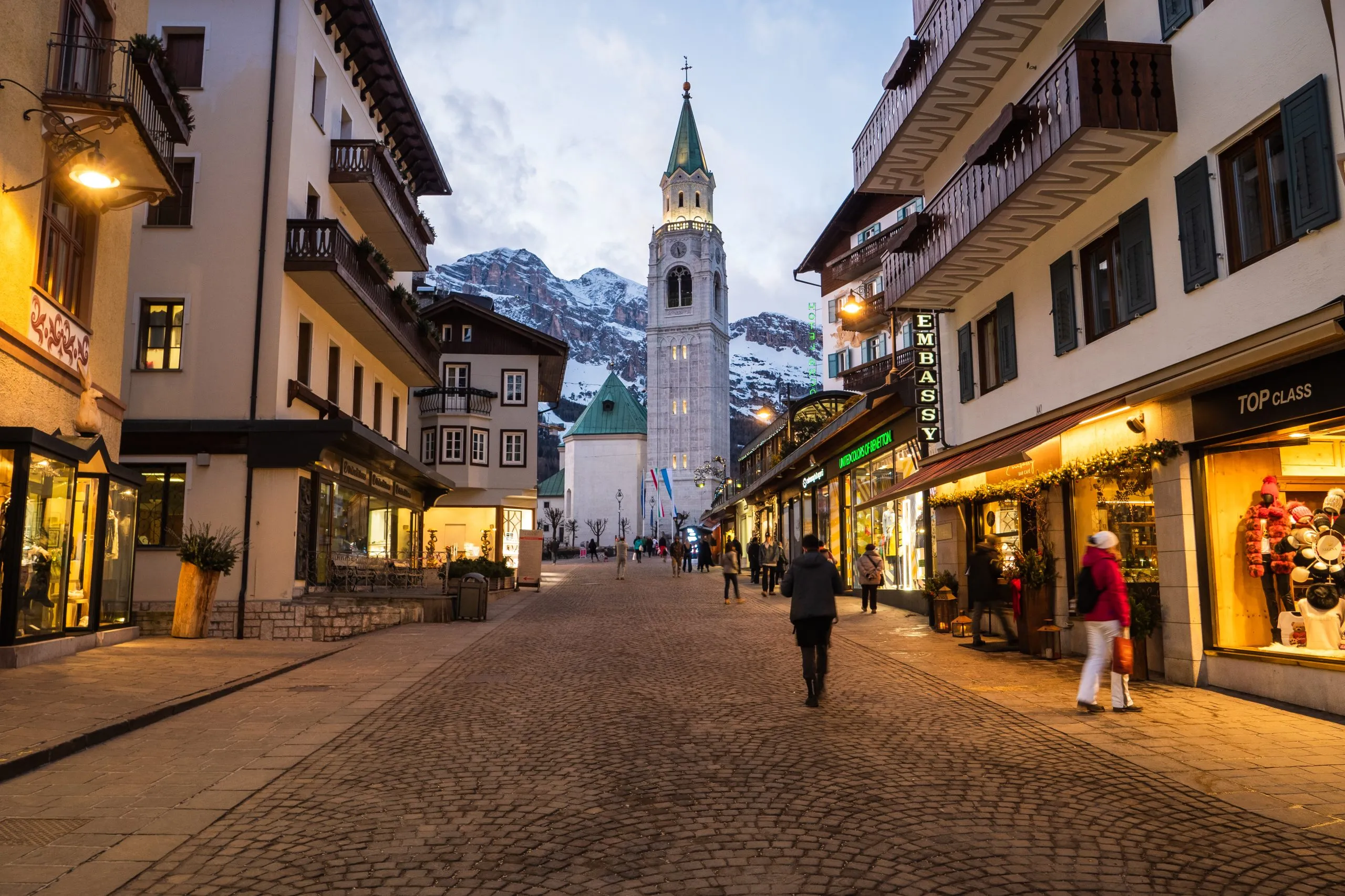 Cortina d'Ampezzo, Italy - February 3 2020: Corso Italia in the Famous Ski Resort Cortina d'Ampezzo on a Winter Evening, the Main Shopping Street in the City Center, with the Spire of the Church